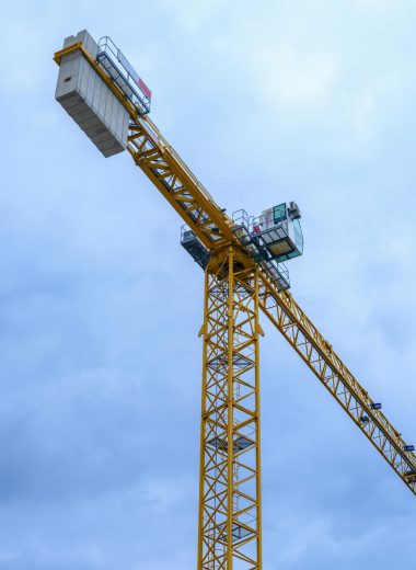 Yellow tower crane with metal structure against a cloudy blue sky.